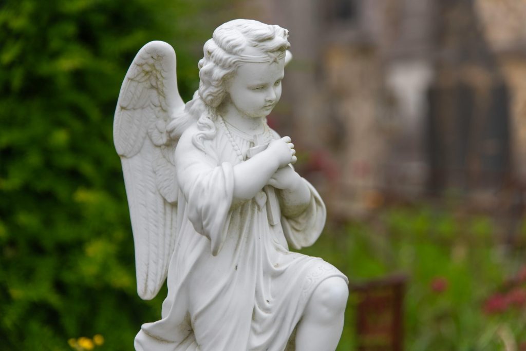 Eine zierliche weiße Engelsstatue in einem Garten im Freien, die Frieden und Spiritualität ausstrahlt.